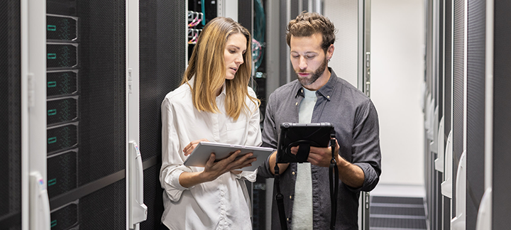A man and a woman are working on a tablet in a server room 
