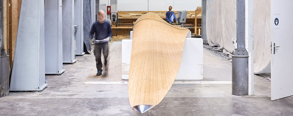 Two people in workshop inspecting and working on a large curved wooden component for industrial use