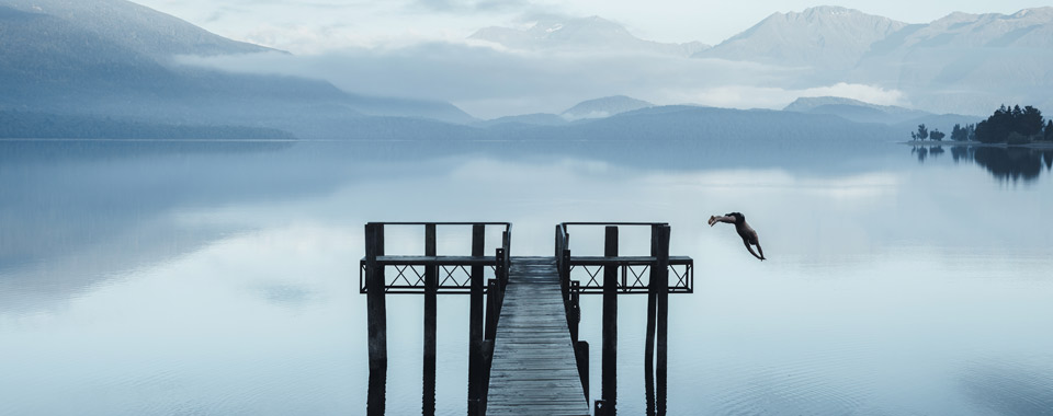 Person springt von einem Steg in einen Bergsee