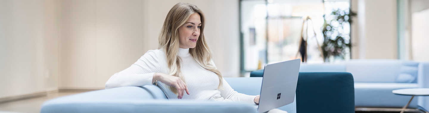 Eine blonde Frau arbeitet in einem Büro an einem Surface-Laptop.