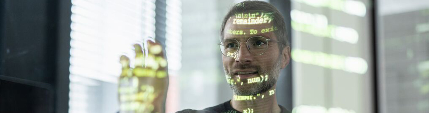 Man wearing glasses focused on programming code displayed on a transparent screen in a modern office