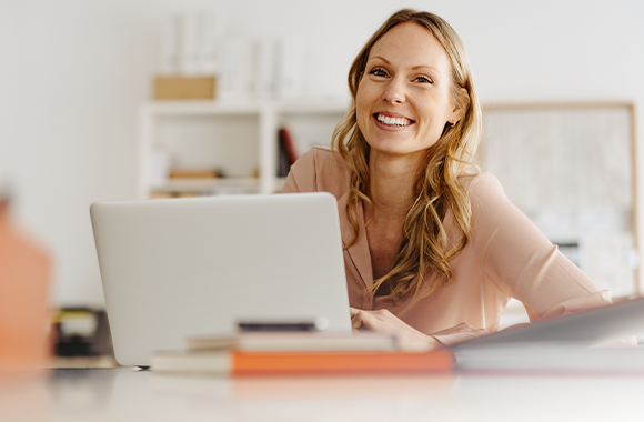 Eine glückliche Frau arbeitet in der Schule an einem Laptop.