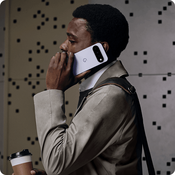 Person im Trenchcoat telefoniert unterwegs mit Smartphone und hält Coffee-to-go-Becher in der Hand
