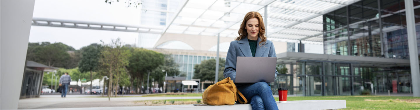 Snapdragon X Series - Woman with Notebook sitting in front of a large office building
