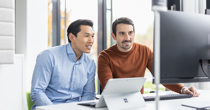 Two smiling men in front of a desktop screen and a tablet.