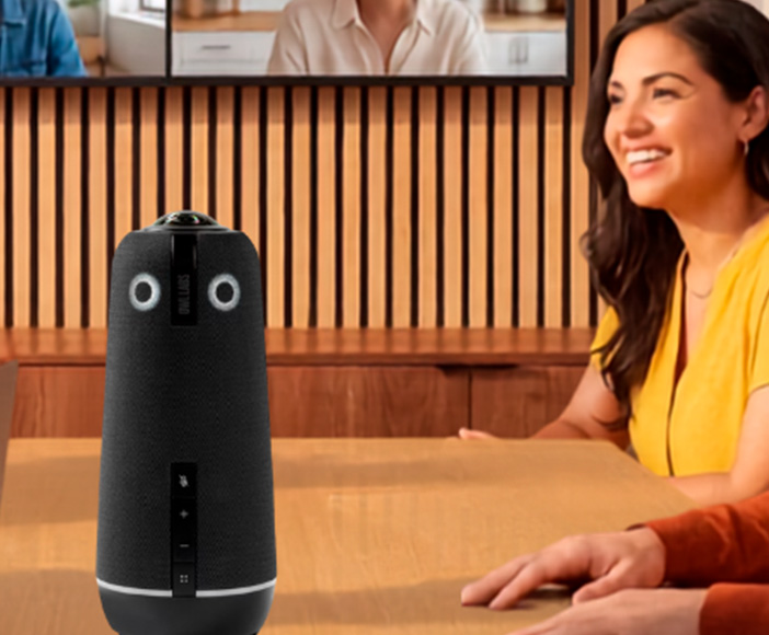Four people in a meeting room conducting a video conference with a Owl Labs amera for virtual collaboration