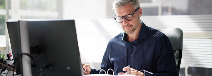 Mann arbeitet konzentriert am Schreibtisch mit Computer und Unterlagen in modernem Büro
