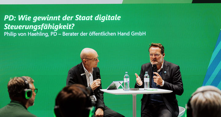 Zwei Experten im Gespräch auf einer Bühne über digitale Steuerungsfähigkeit des Staates bei einer Fachveranstaltung