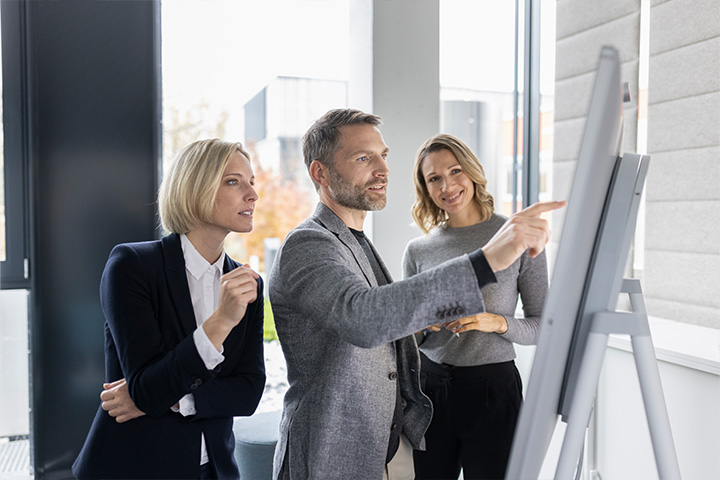 3 leute sehen sich ein whiteboard an