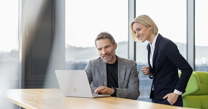 Ein Mann und eine Frau blicken zufrieden auf einen Laptop