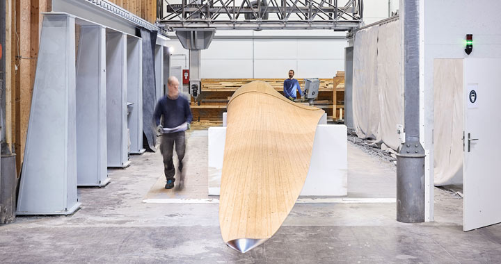 Two people in workshop inspecting and working on a large curved wooden component for industrial use