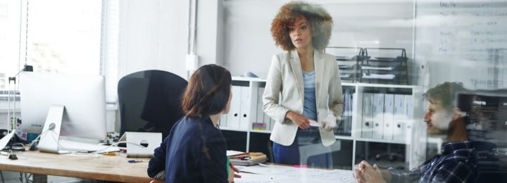 Drei Personen im modernen Büro diskutieren gemeinsam an einem großen Tisch mit Dokumenten und Computern