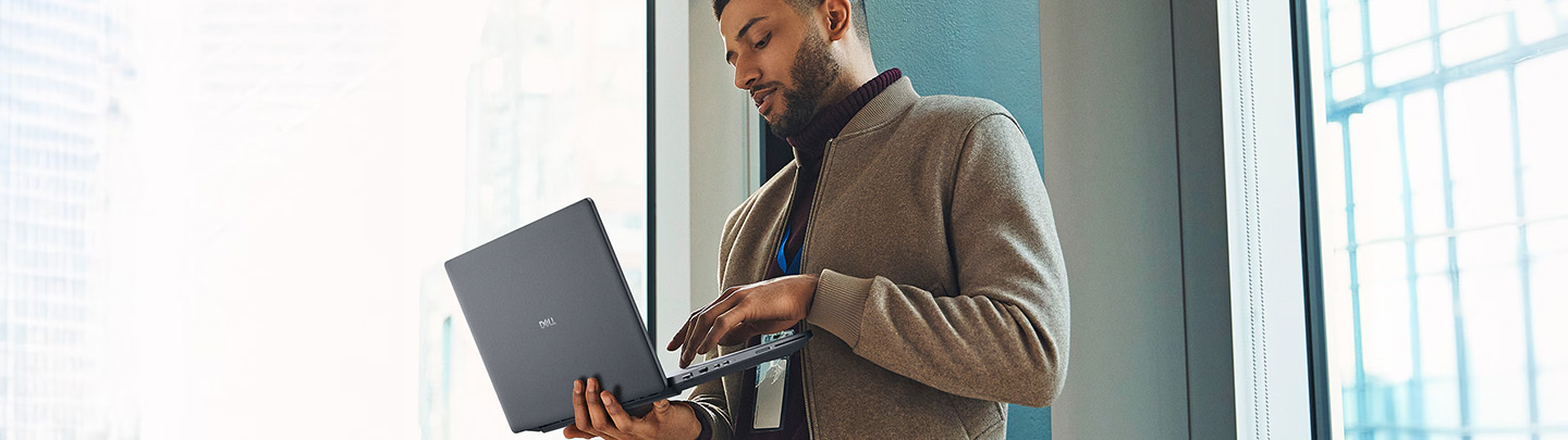 Man standing by window working focused on a laptop in a modern office environment