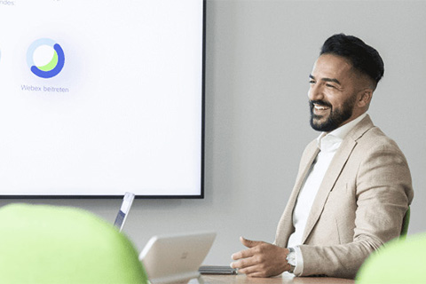 Ein Bild von einem Mann der lächelnd in einem modernen Meeting-Raum sitzt.