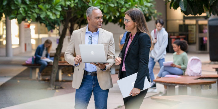 A man and a woman on the street, holding laptops