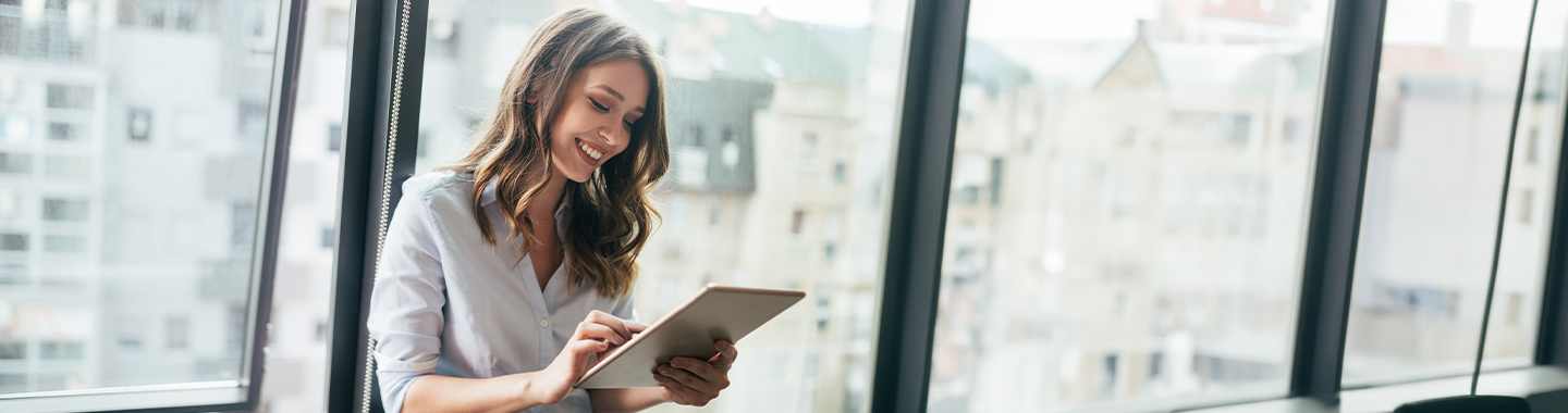 A woman smiles and uses a tablet in the office
