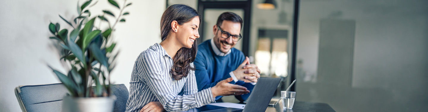 Zwei Personen in einem modernen Büro, die gemeinsam an einem Laptop Inhalte besprechen, um zusammenzuarbeiten