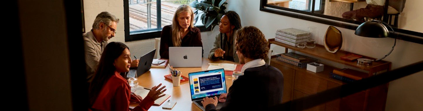 Team discussing together at a table in a modern office with Apple laptops and a presentation on screen